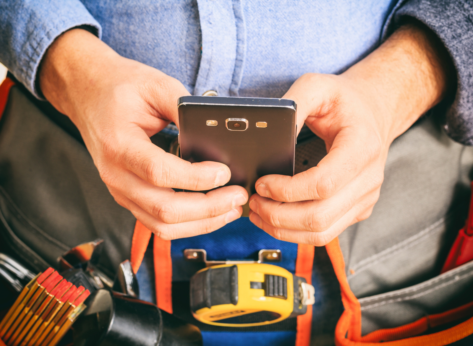Profile of builder with tool belt completing a Punch List Form on smart device: NestForms punch list form construction