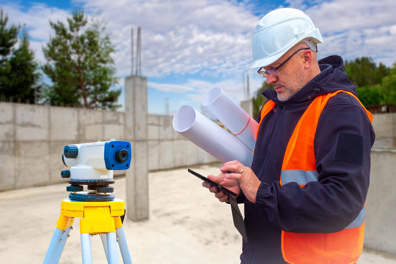 Land Surveyor holding smart device, working with other topographic and geodetic tools: The NestForms GPS Land Survey App