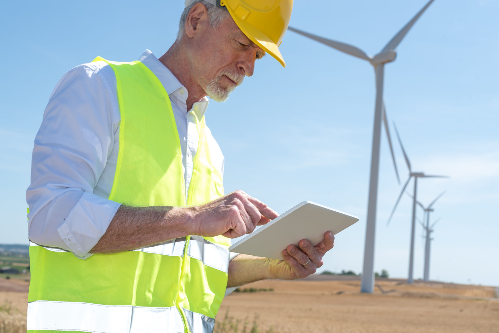 An inspector in safety gear in front of wind turbines working on a checklist form: NestForms final inspection checklists