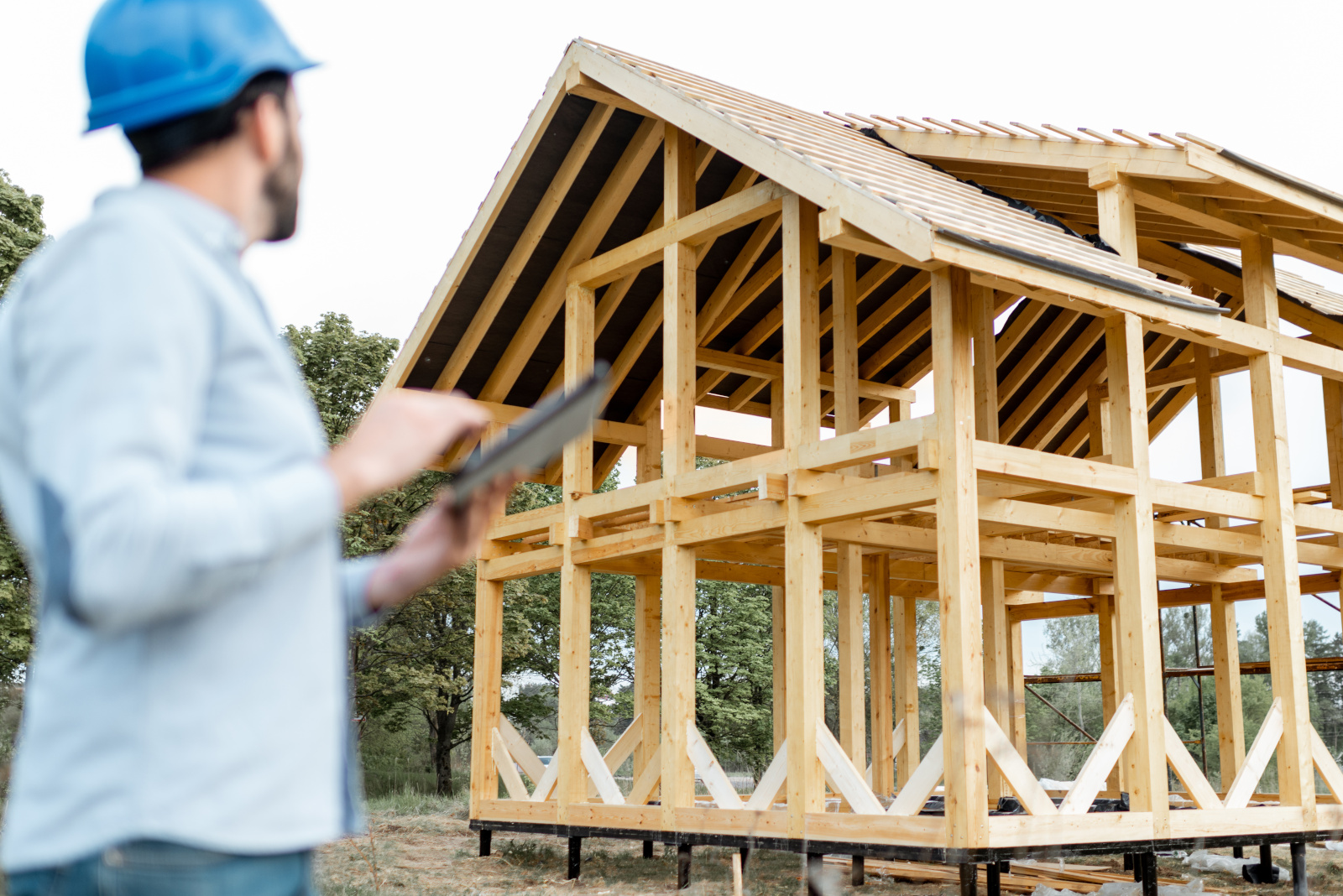 Construction worker with tablet in front of a skeleton timber framed home: Frame Homes UK and NestForms Offline Survey