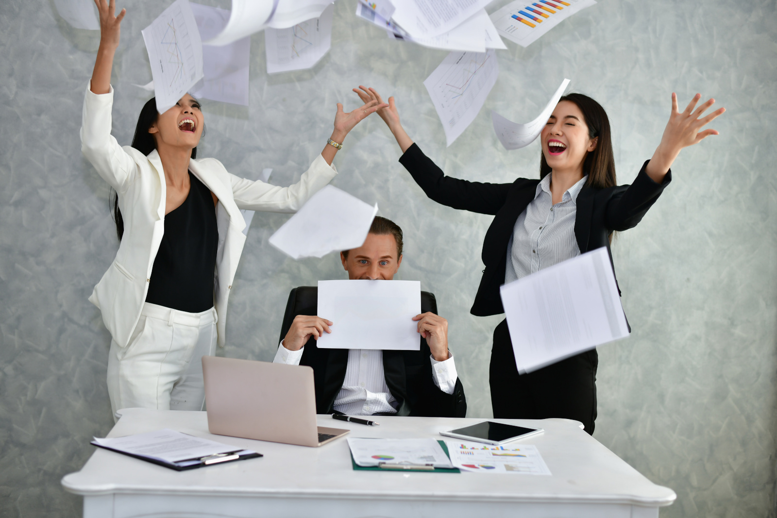 Three office workers at desk with laptop and tablet scattering paper forms in the air: The NestForms Mobile Survey App