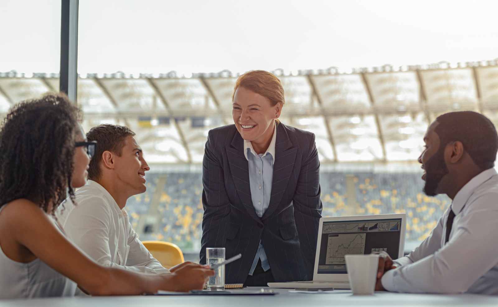 Business Meeting with Colleagues at Stadium Location, colleagues are completing a handover form on laptop