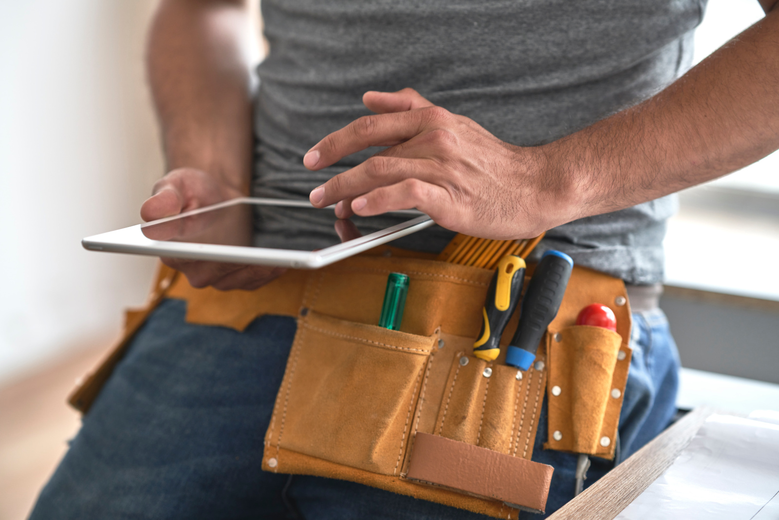A construction worker with tool belt and holding tablet completing a New Build Snagging Checklist form with NestForms 