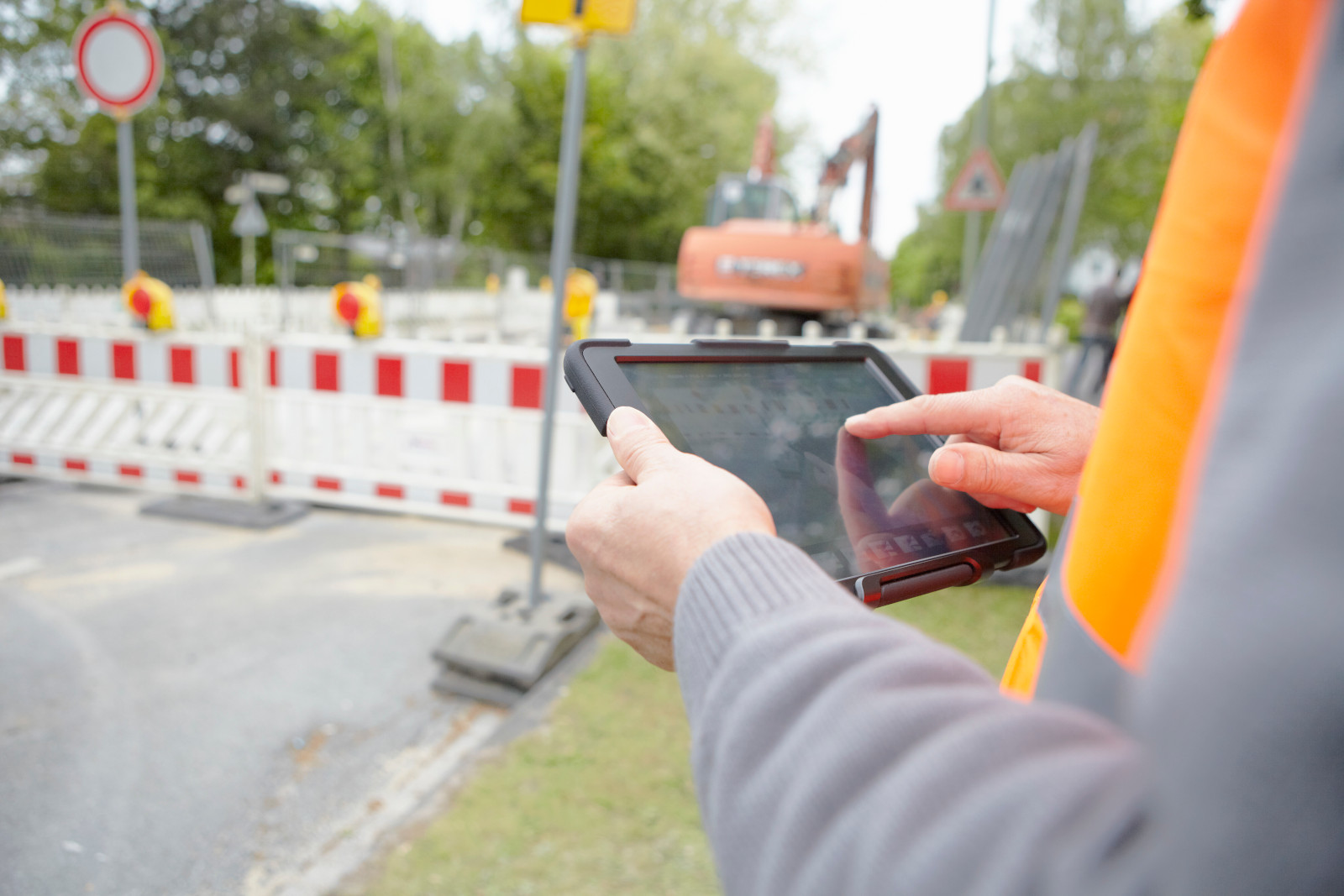 Close up of foremans’ hands, at an urban road construction site and holding smart device: the NestForms Offline Survey App