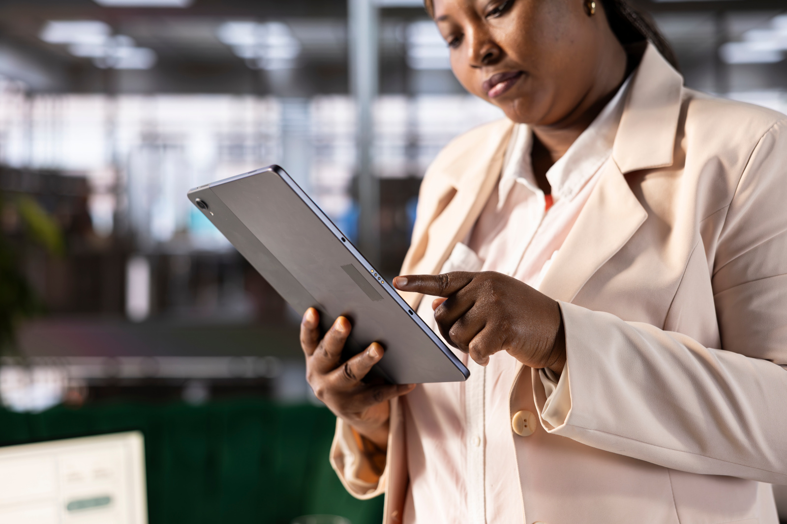 Close up of Woman in a pink suit standing up in an office, while managing a digital survey with tablet.