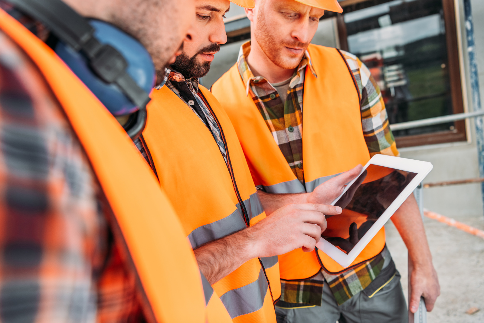 Group of construction workers in hi-vis clothing looking at tablet: The NestForms Field Service Management Software