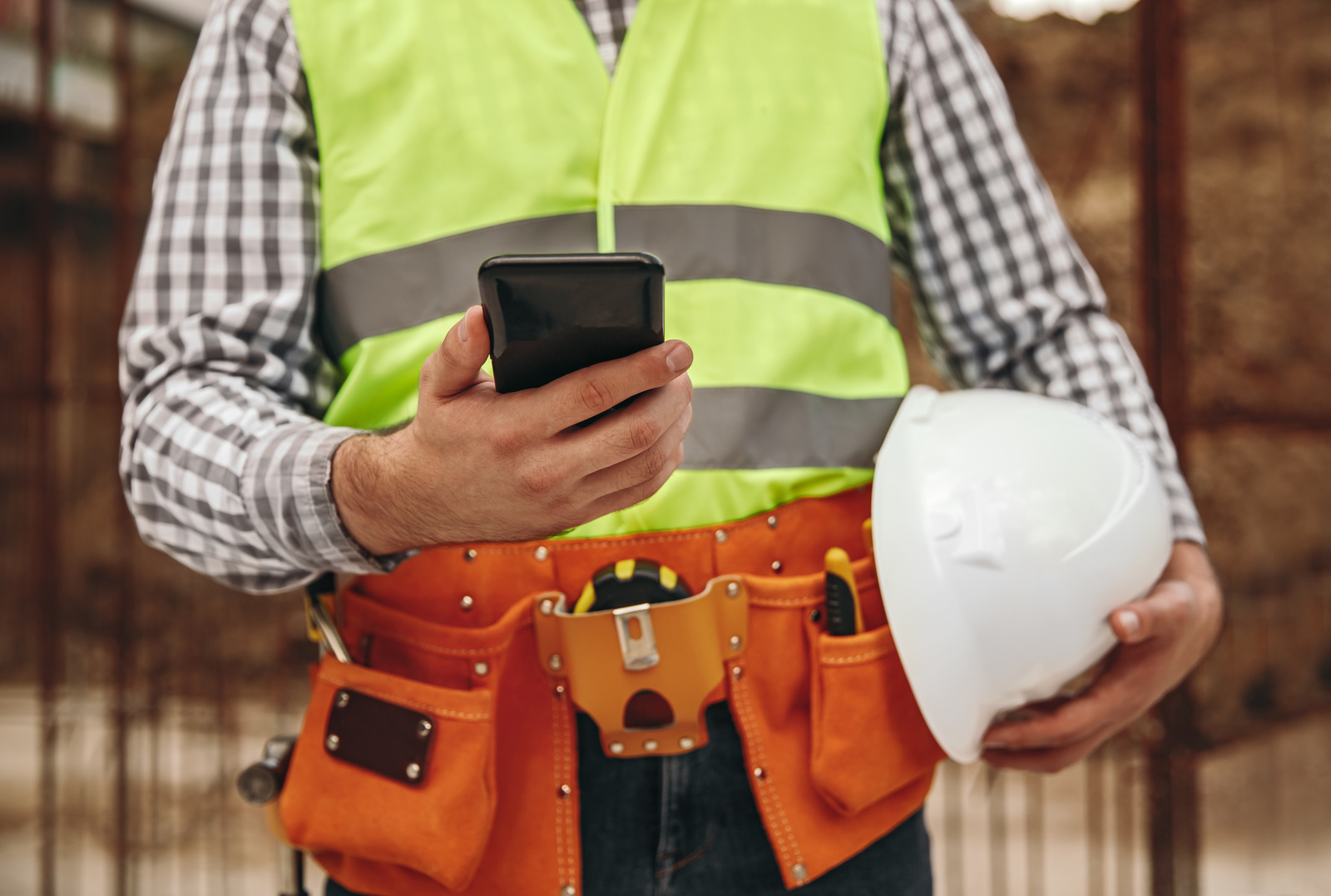Construction contractor with tool belt and safety helmet holding smart device: the NestForms Punch List App