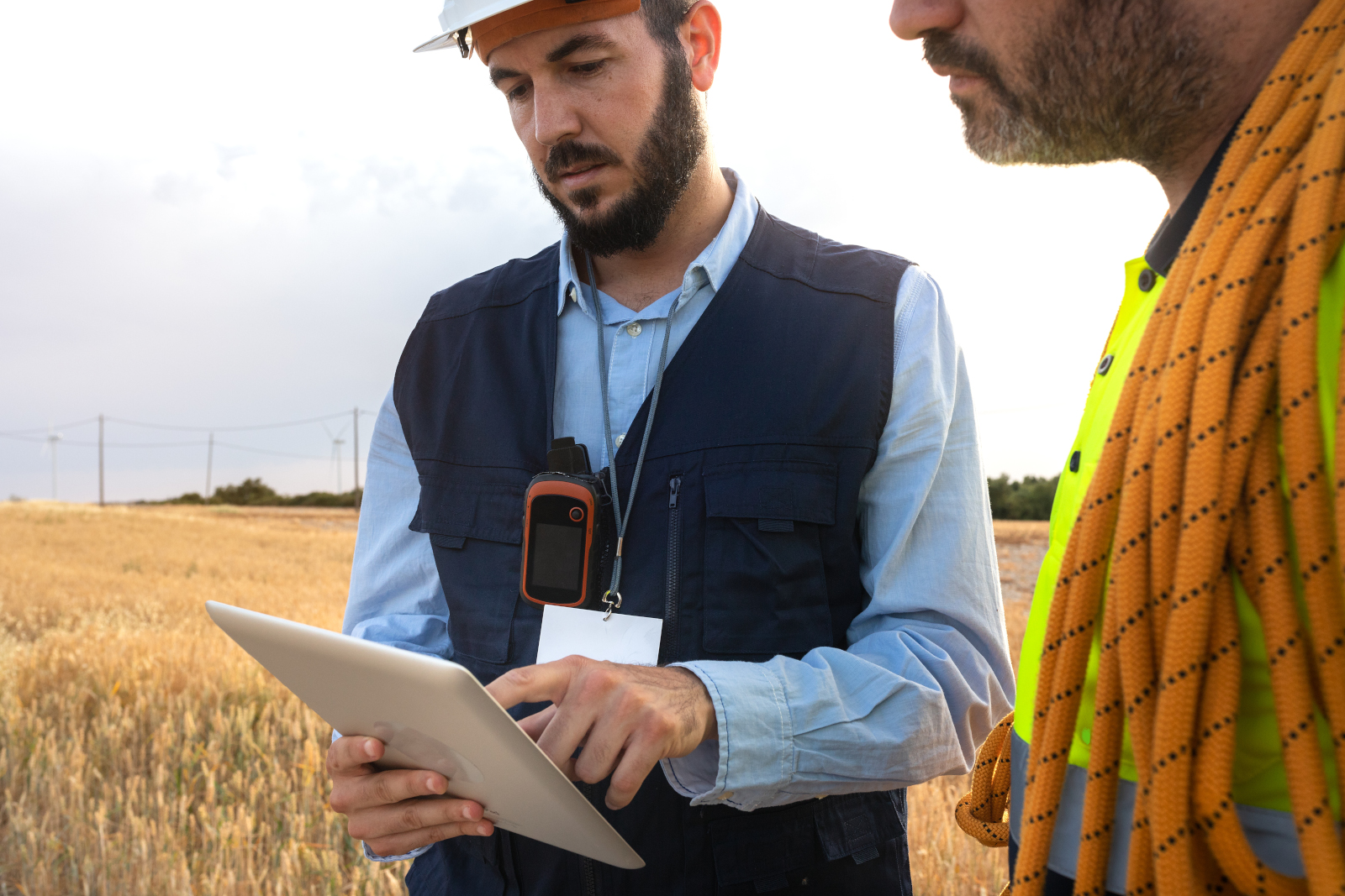 Two Land surveyors in safety gear working in open countryside using a smart device: The NestForms Land Survey app