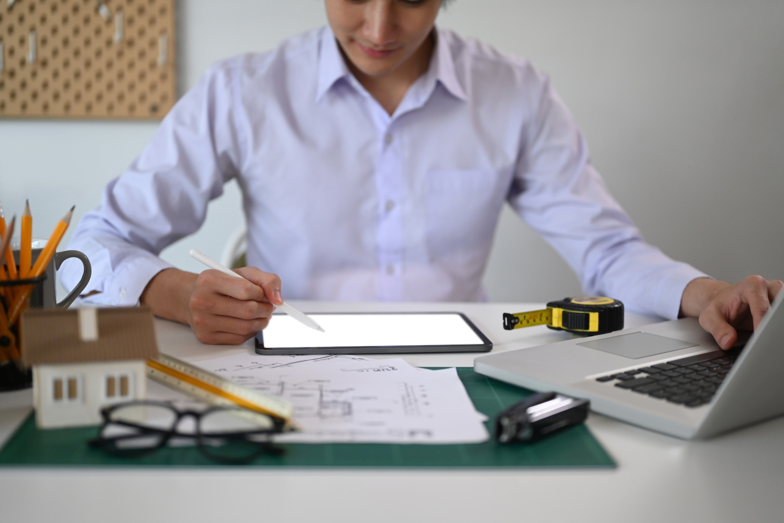 Project Manager at desk with laptop and utensils making a digital sketch on a tablet with the NestForms surveying app