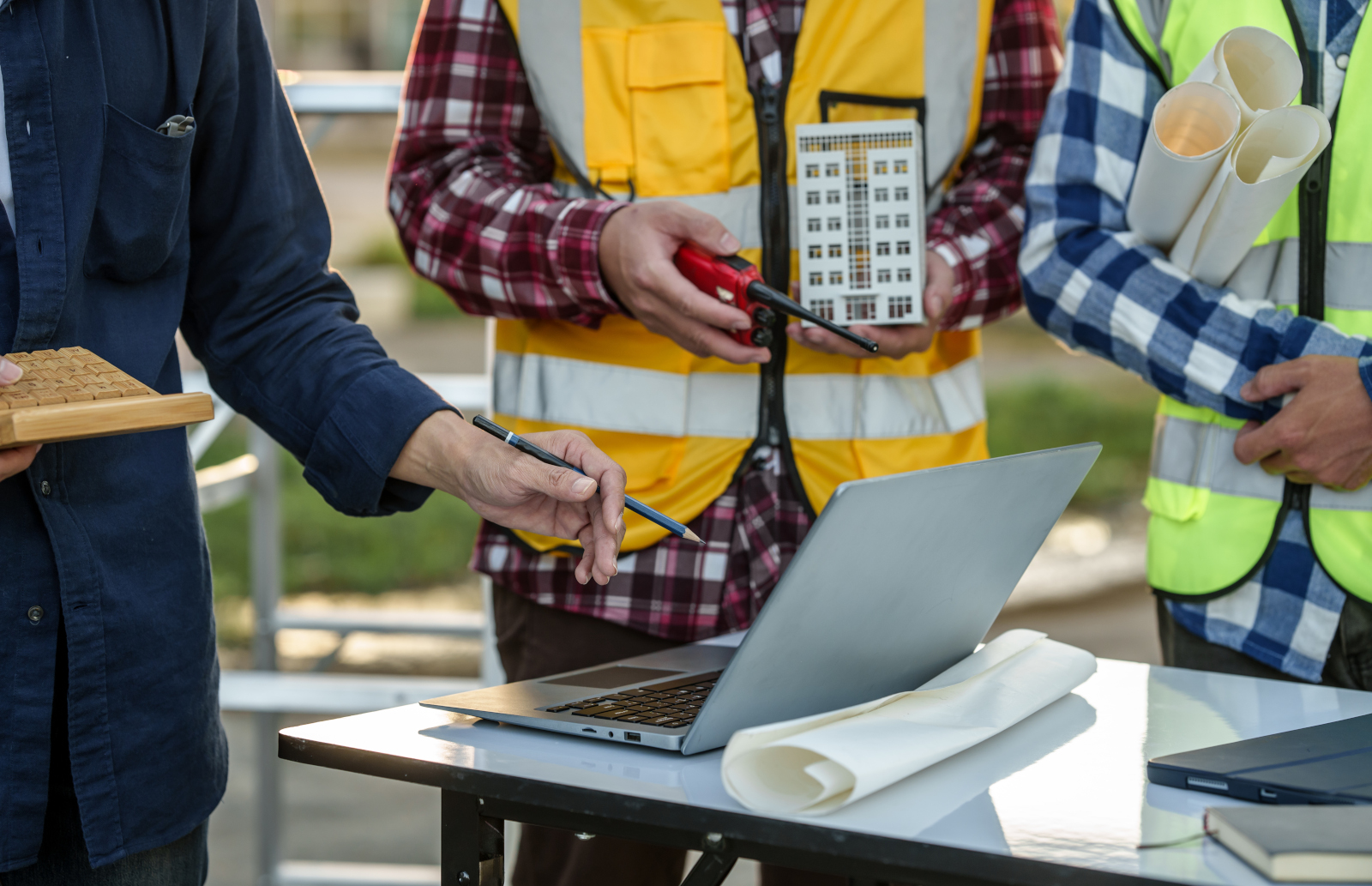 Three land surveyors at table with laptop and smart device, maps and other surveying gear: The NestForms GPS Land survey app