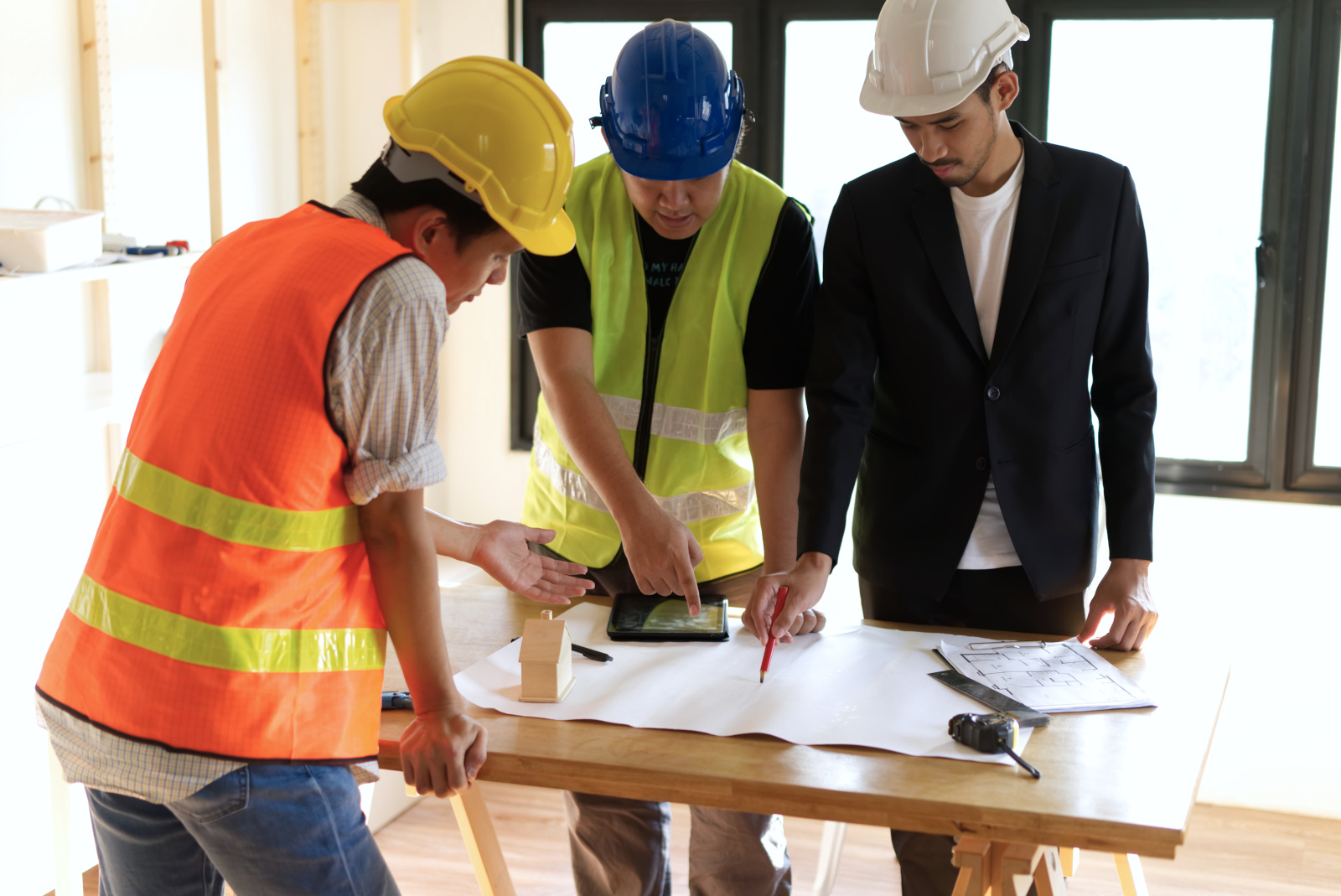 Three man construction team at table with tablet and paper plans discussing project: The NestForms field management system