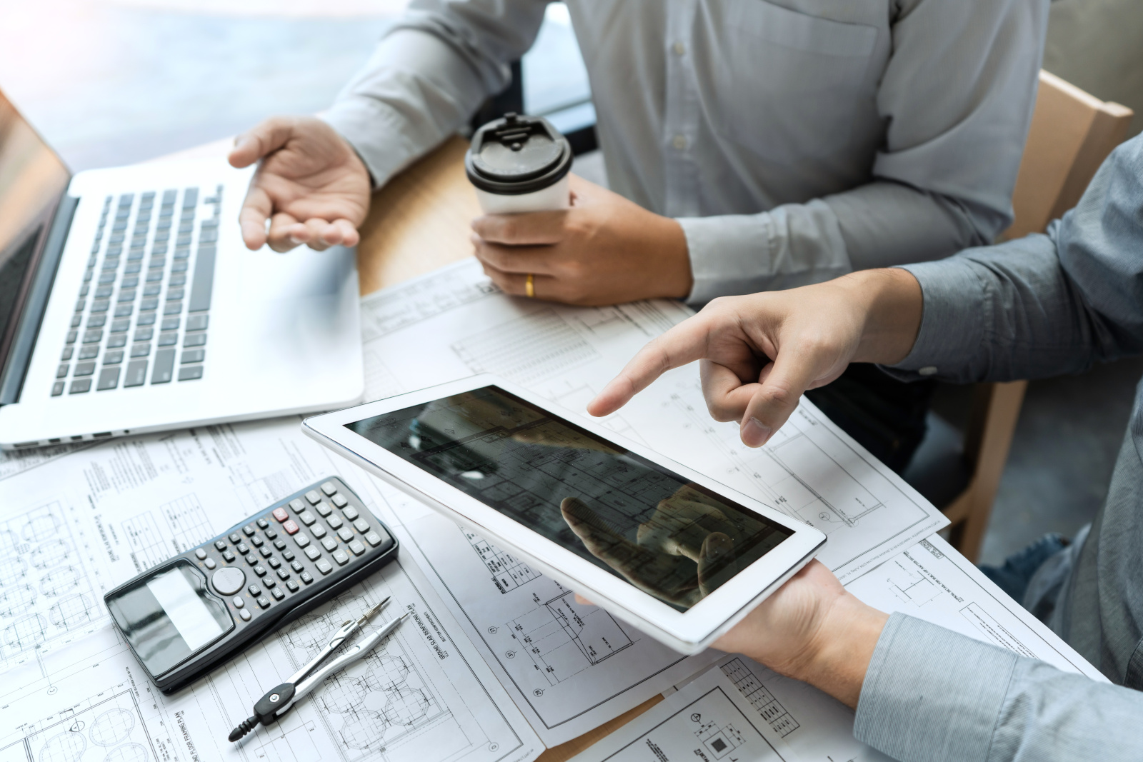 Project management team in office at desk with plans, tablet and laptop: Project Handover Checklists with NestForms