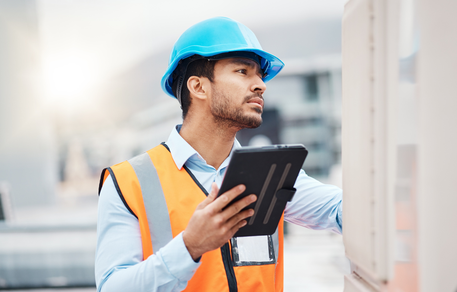 Construction manager in hi-vis and safety helmet with tablet completing a snagging list survey: NestForms offline surveys
