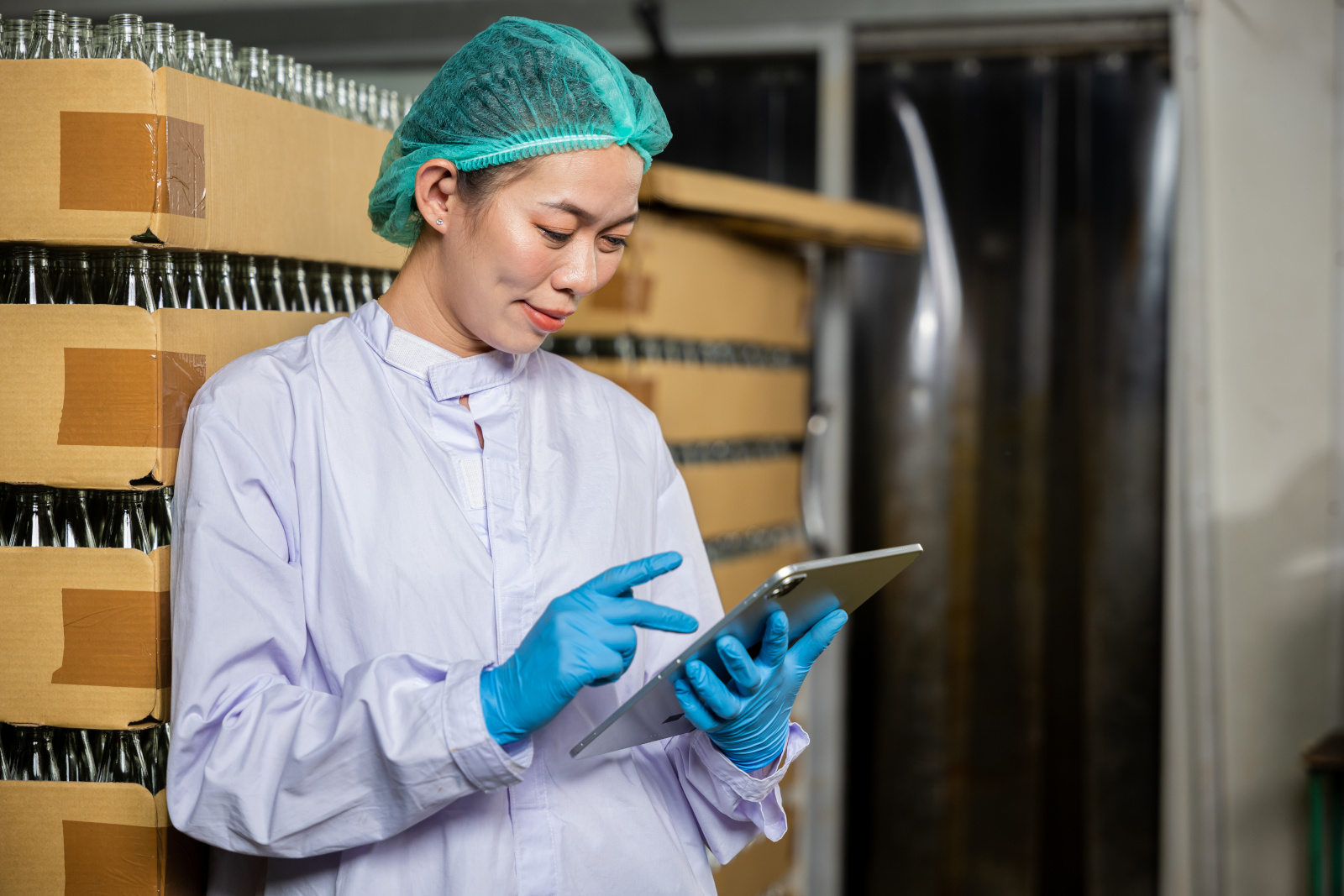 Female Quality Control inspector with tablet standing in front of a pallet of bottles: The NestForms Quality Control app