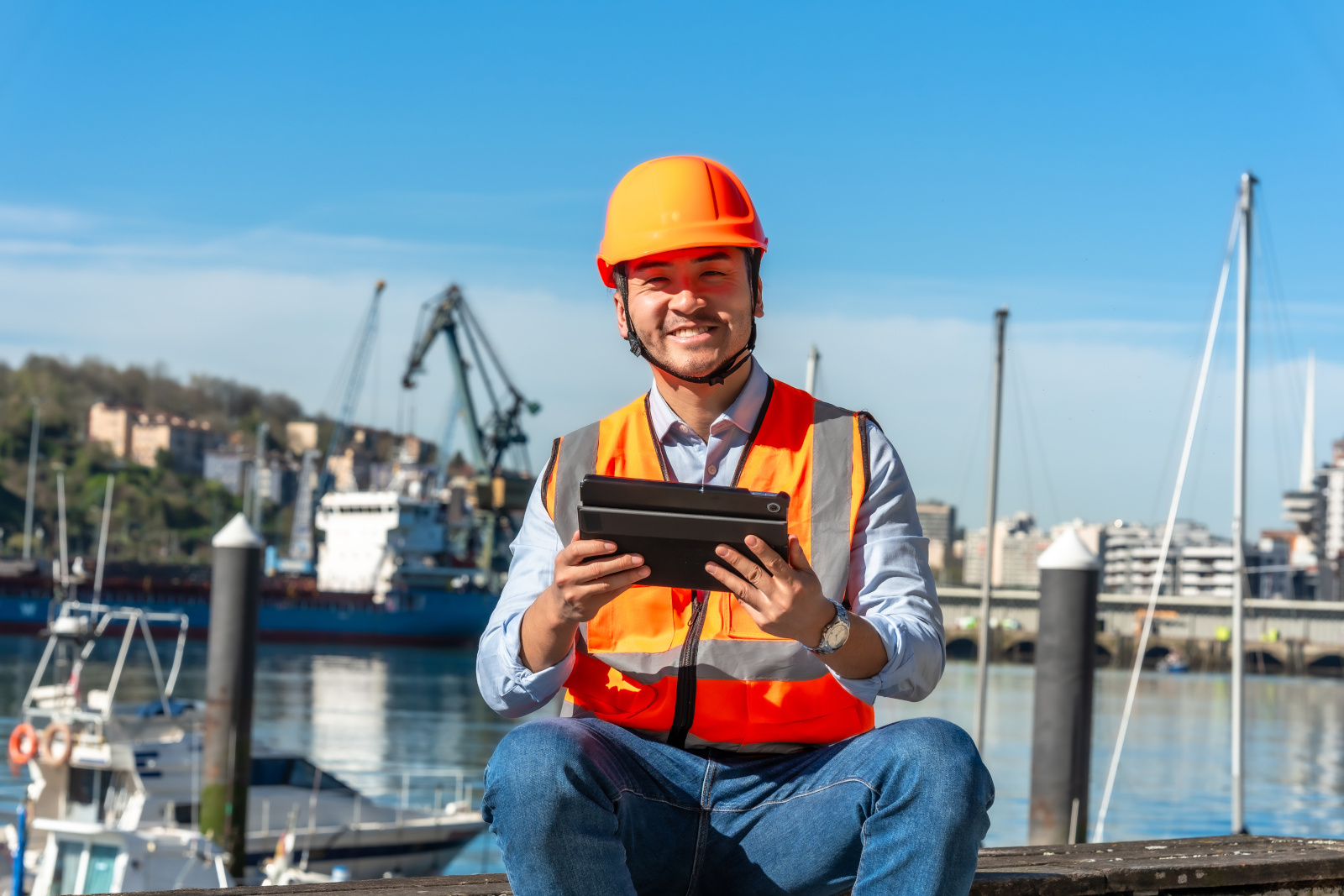 Happy surveyor at a port in hi-vis vest and safety helmet holding tablet: The NestForms field management system