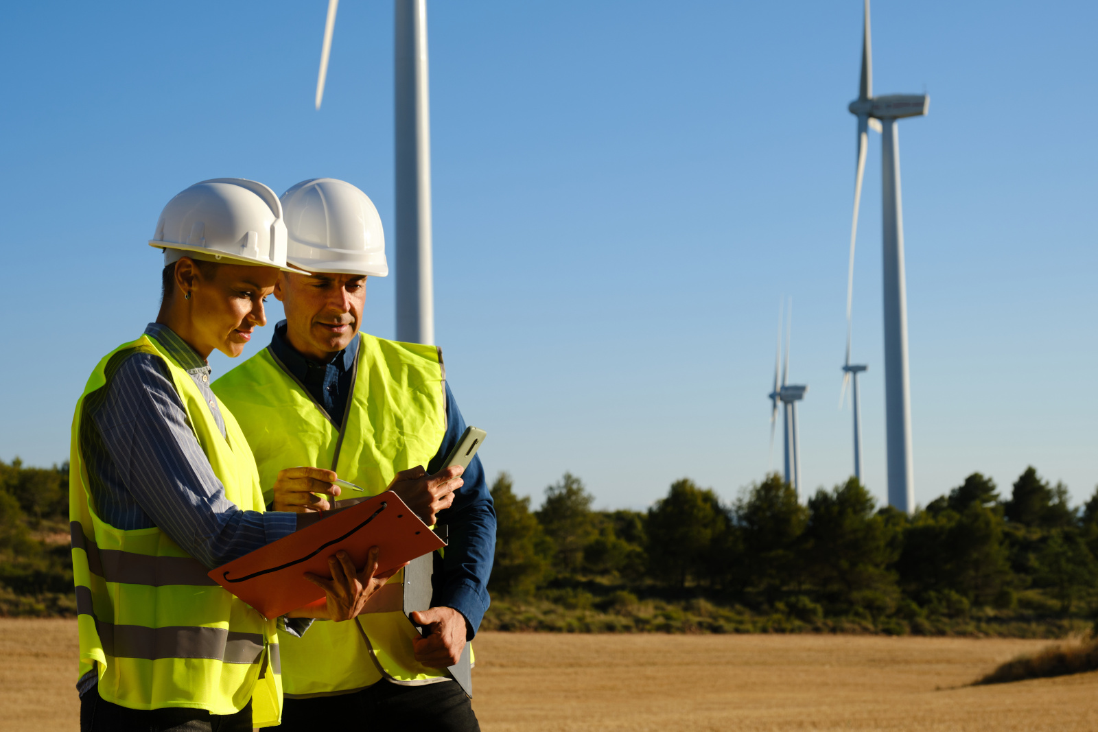 Two wind turbine project managers outdoors in safety gear with smart device working on a NestForms Project completion form
