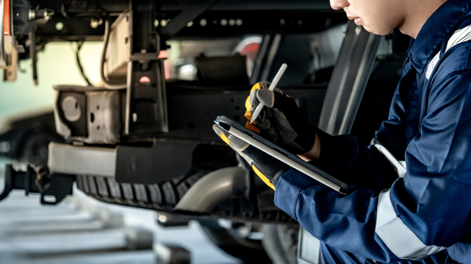 Mechanic with smart device at vehicle safety testing centre using NestForms mobile form app to check underside of vehicle